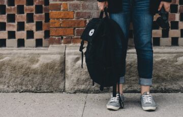 young person in jeans holding a black backpack