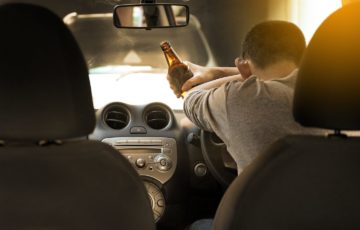 Person asleep inside their car with a bottle of beer. Stechschulte Nell law