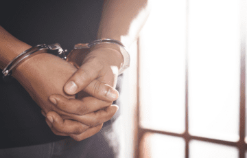 Man in handcuffs standing behind bars