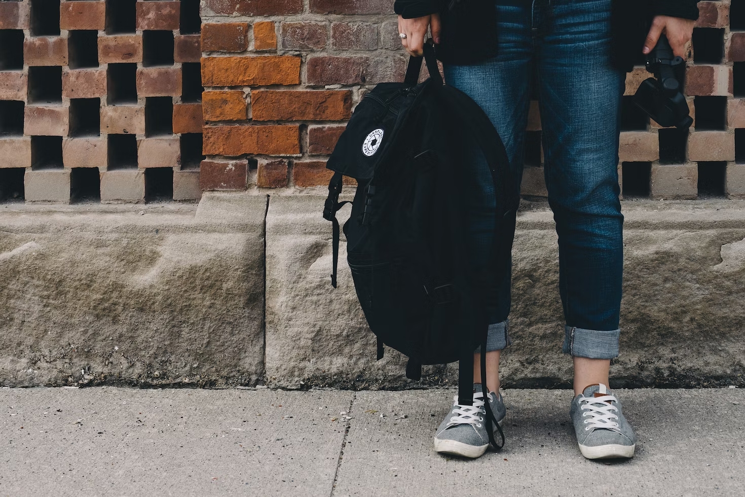 young person in jeans holding a black backpack