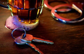 glass of alcohol next to keys and handcuffs