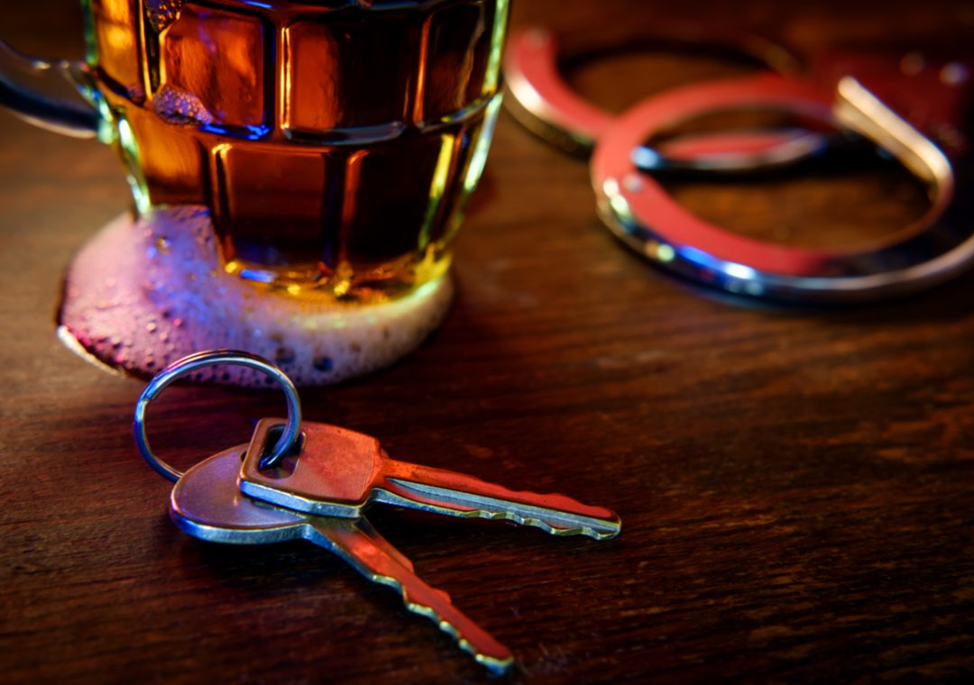 glass of alcohol next to keys and handcuffs
