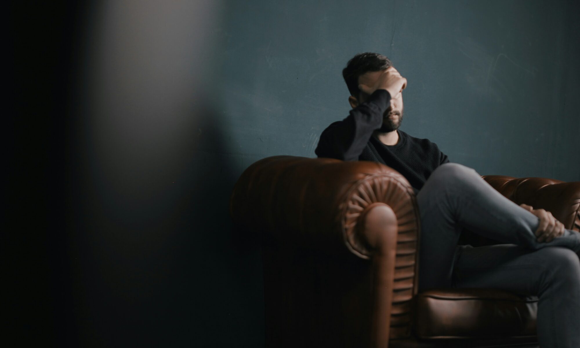 man sitting on couch holding head