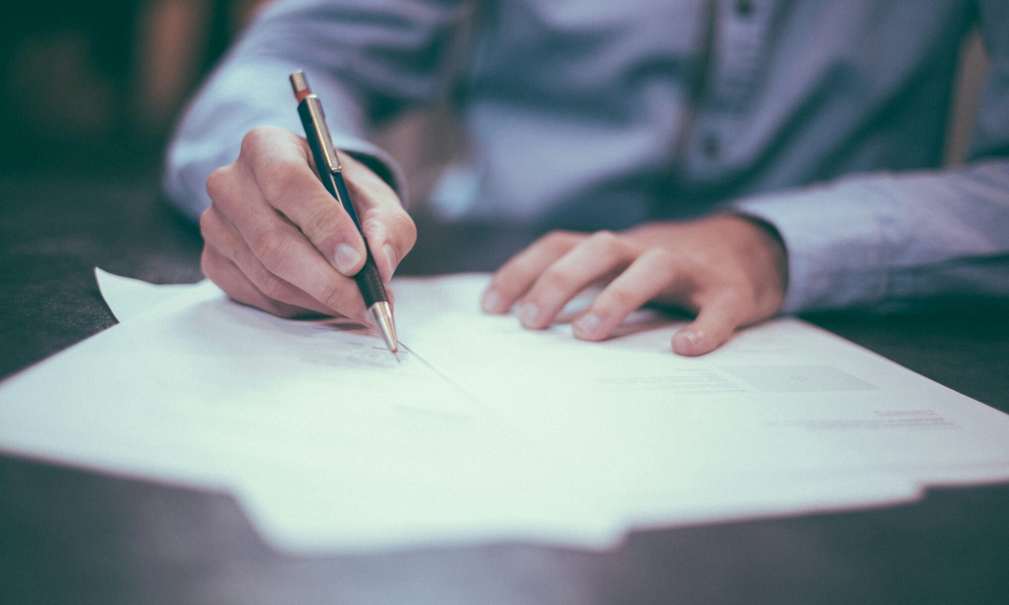 man writing on a stack of papers on a desk